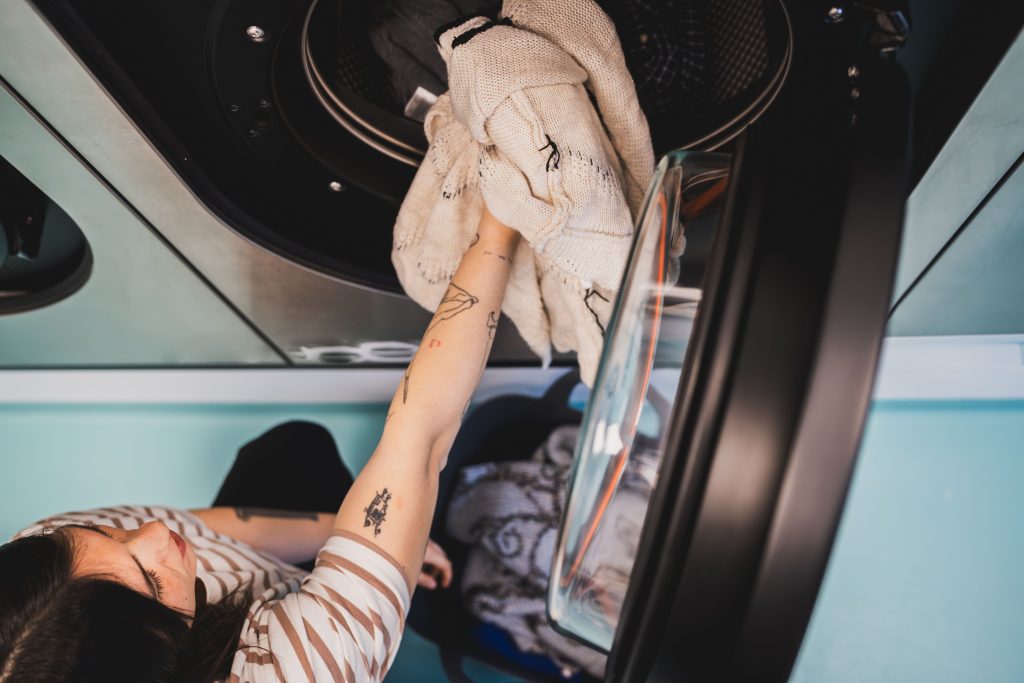 Young woman taking out clean clothes from washing machine in a turquoise laundry room